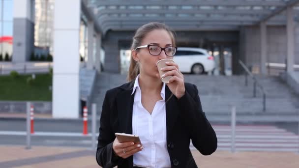 Schöne Geschäftsfrau mit Smartphone trinkt Kaffee auf der Straße gegen Büro. Steter Schuss - Filmmaterial, Video