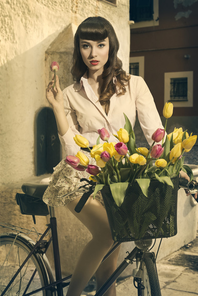 sexy retro pin-up on bike in old town with tulips - Foto, imagen