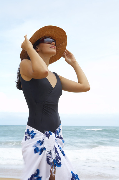 Вид симпатичной женщины в черном купальнике, держащей соломенную шляпу
 - Фото, изображение