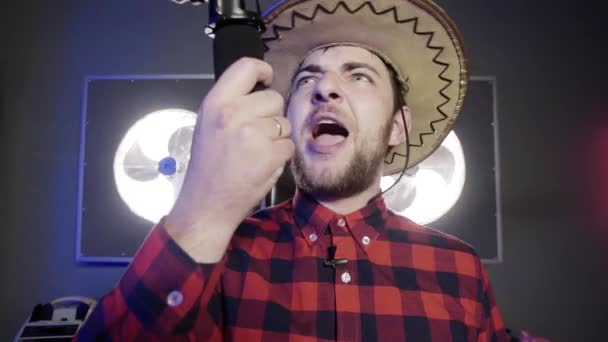 Przystojny szary Eyed Brodaty facet ubrany meksykański kapelusz trzyma mikrofon i śpiewa. - Materiał filmowy, wideo