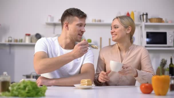Handsome man feeding girlfriend with cake, date in kitchen, romantic atmosphere - Кадры, видео