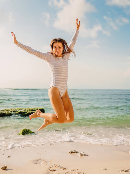 Jumping happy woman in swimsuit on ocean beach at sunset. Summer holidays - Фото, изображение