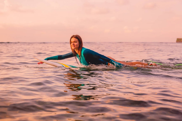 Surfgirl with perfect body on a surfboard floating in ocean. Surfing at sunset - Photo, image