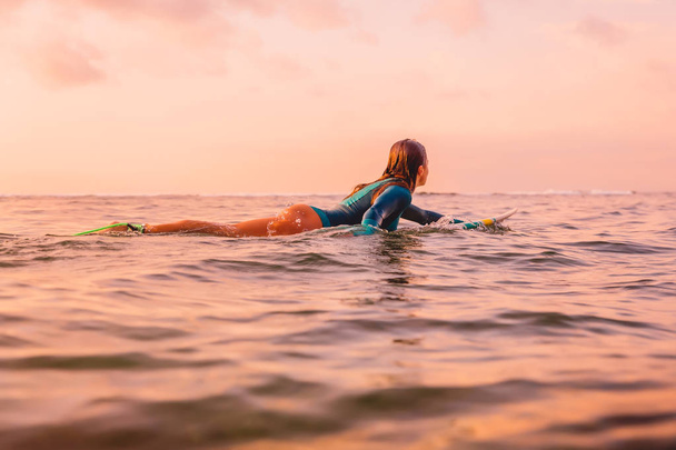 Surfgirl mit perfektem Körper auf einem im Meer treibenden Surfbrett. Surfen bei Sonnenuntergang - Foto, Bild