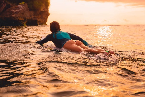 Surfgirl with perfect body on a surfboard floating in ocean. Surfing at sunset - Photo, Image