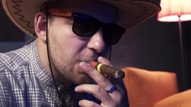 arroganter Kerl mit Sonnenbrille und mexikanischem Hut raucht teure kubanische Zigarre - Filmmaterial, Video