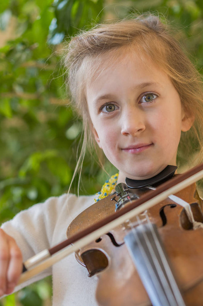 Nahaufnahme eines Kindes, das Geige spielt, auf grünem Hintergrund. Porträt eines Mädchens mit Saite und Geige. Porträt der kleinen Geigerin. schönes begabtes kleines Mädchen, das auf Geige spielt - Foto, Bild