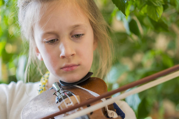 Zár-megjelöl-ból egy gyermek hegedül zöld háttér. Lány string és játék hegedű portréja. A kis Hegedűs portréja. Gyönyörű, tehetséges kislány játszott hegedűn. - Fotó, kép