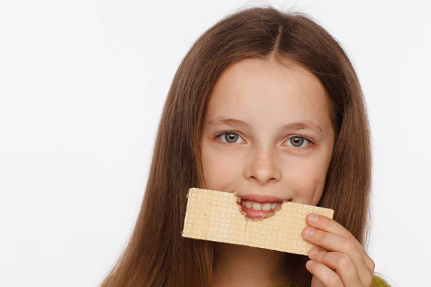 Portrait of a beautiful 8 year old girl in a sweater and with a wafer in her hand. White background - Φωτογραφία, εικόνα