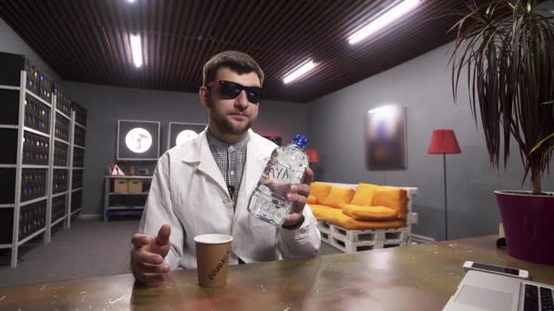 Charismatický chlapík v bílém laboratorním plášti nalévá vodu z plastové láhve na papírový pohár - Záběry, video
