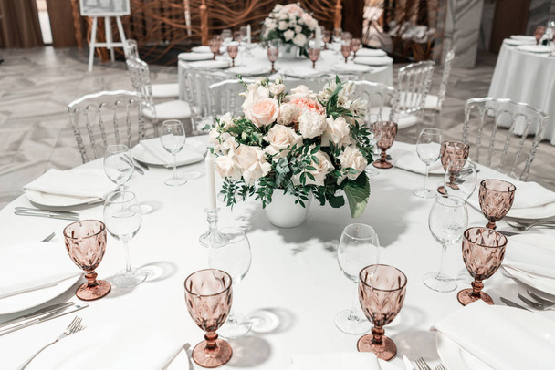 Flower arrangement in the center of the table. Interior of restaurant for wedding dinner, ready for guests. Round Banquet table served. Catering concept. - Photo, Image