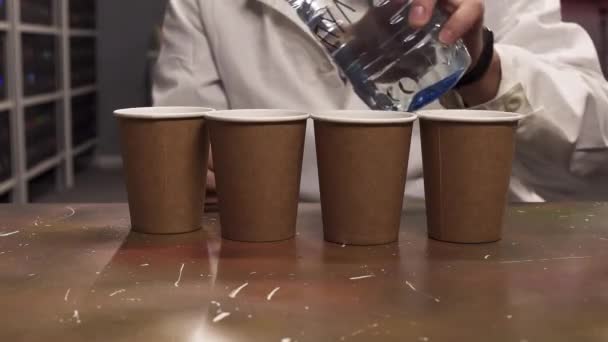 Man draagt witte Lab vacht gietwater uit plastic fles tot vier papieren bekers - Video