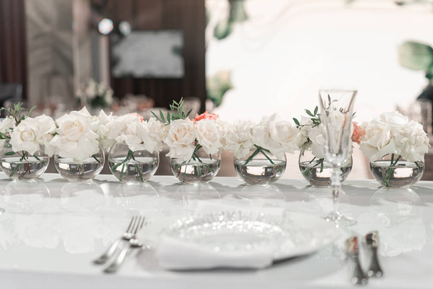 ボールガラスの花瓶に小さな花の配置。新婚夫婦のテーブル結婚式のディナーのためのレストランのインテリア、ゲストのための準備ができています。ケータリングコンセプト. - 写真・画像