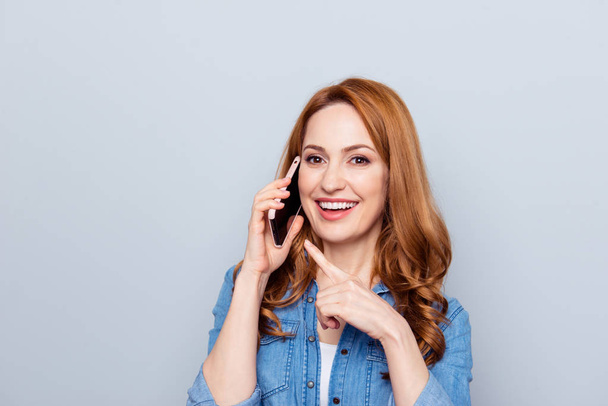 Close up photo beautiful she her curly foxy lady arm hand telephone speak tell friends interested curious direct indicate app pda finger wear casual blue jeans denim shirt isolated grey background - 写真・画像