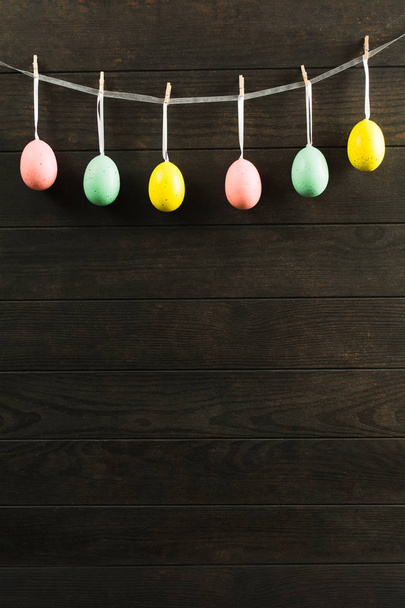 Пасхальные пастельные декоративные яйца с лентой на веревке на деревянном фоне
 - Фото, изображение
