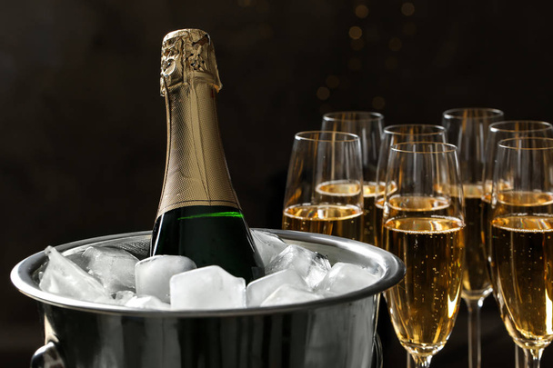 Bottle in bucket with ice near glasses of champagne on dark background - Foto, Imagen
