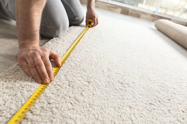 Man measuring carpet indoors, closeup view. Construction tool - Foto, Bild