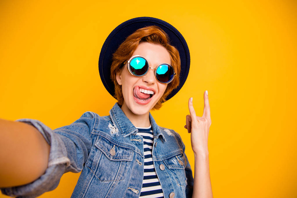 Close up photo funny funky foxy she her lady make take selfies metal music lover tongue out mouth wear specs vintage hat casual striped t-shirt jacket jeans denim isolated yellow bright background - Фото, изображение