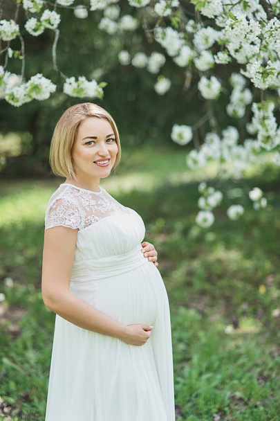 Весеннее настроение, красивая беременная женщина запах цветущей вишни, наслаждаясь природой, белый цветочный сад
. - Фото, изображение