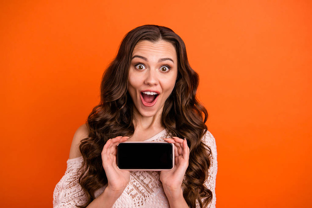 Close-up portrait of nice-looking attractive lovely feminine girlish toothy funny cheerful cheery wavy-haired lady holding in hands new cool device isolated over bright vivid shine orange background - Fotografie, Obrázek