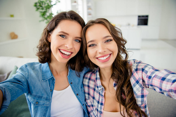 Close up photo beautiful amazing she her cute ladies buddies make take selfies funky cheerful toothy wear casual jeans denim checkered plaid shirts apartments sit comfy divan couch room indoors - Foto, Imagen