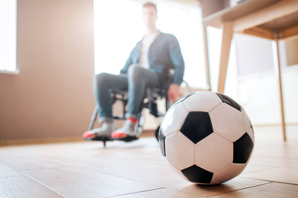 Young man with disability sitting on wheelchair and look down at ball for game. Ex sportsman. Upset and unhappy. Trauma. Cant play football anymore. - Φωτογραφία, εικόνα
