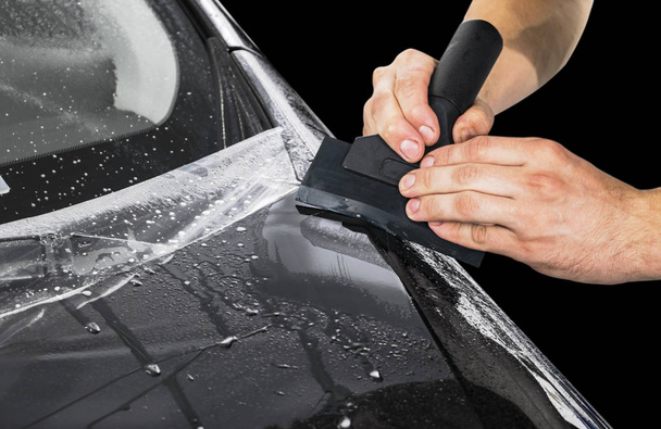 Car wrapping specialist putting vinyl foil or film on car. Protective film on the car. Applying a protective film to the vehicle with tools for work. Car detailing. Transparent film. Car paint protection.  - 写真・画像