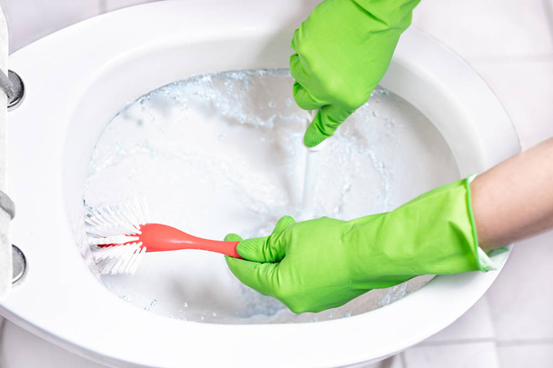 Θηλυκό χέρι σε καουτσούκ γάντι καθαρισμού λεκάνη τουαλέτας - Φωτογραφία, εικόνα