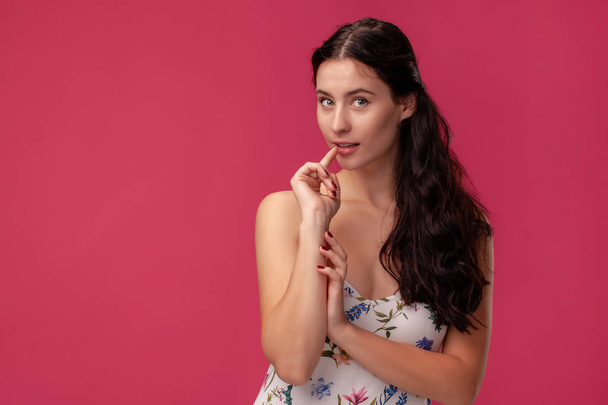 Porträt einer hübschen jungen Frau in einem hellen Kleid, das auf rosa Hintergrund im Studio steht. Menschen aufrichtige Emotionen. - Foto, Bild