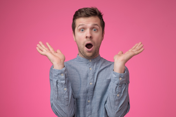 Shocked face of caucasian man in blue shirt on pink background - Photo, Image