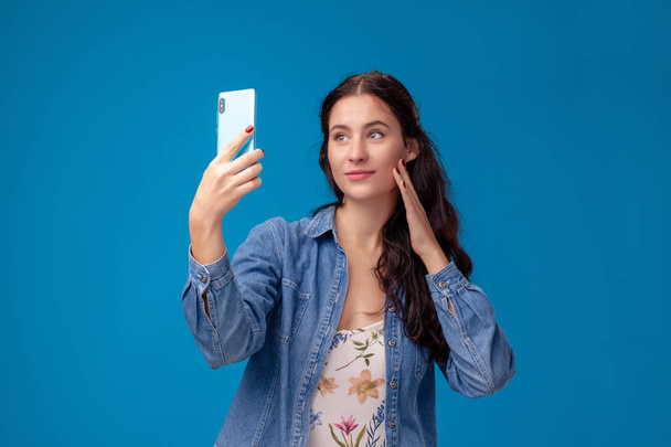 Giovane donna bruna è in posa con uno smartphone in piedi su sfondo blu
. - Foto, immagini
