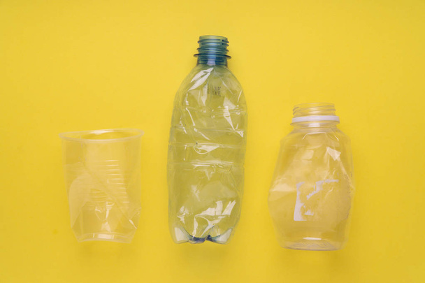 Crashed plastic bottles and a cup on yellow background. Plastic utilisation concept. Ecological problem, global environment. - Foto, Imagem