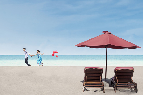 Beautiful couple run near beach chairs and umbrella - Photo, Image