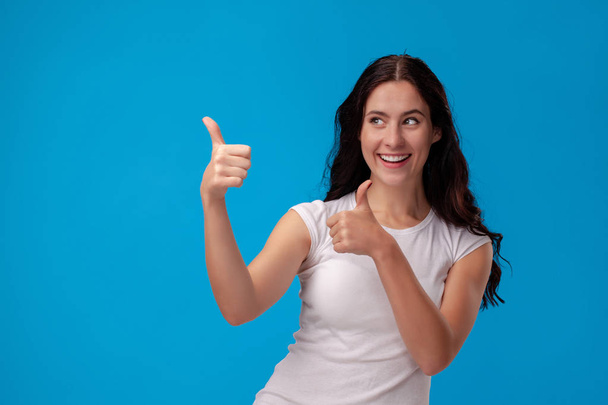 Smiling woman giving thumbs up on blue background - Fotó, kép