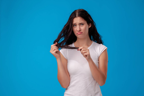 Sad woman is pulling her hair on blue background - Photo, Image