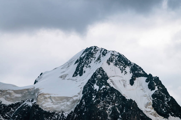 Csodálatos gleccser közelkép. Havas sötét hegytető a felhős égen. Sziklás gerinc havazással borús időben. Csodálatos hegyvonulat a ködben. Fenséges természetű, légköri minimalista táj. - Fotó, kép