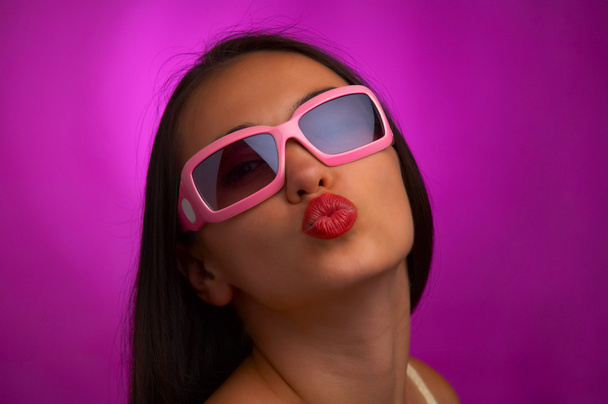 Glamour portret van jonge brunette in roze zonnebril geven een kus - Foto, afbeelding