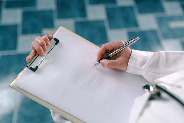 Female doctor in white uniform writing on clipboard paper patient's medical history. Woman as health specialist in exam, er, disease prevention, visit check or healthcare lifestyle concept - Foto, Imagem
