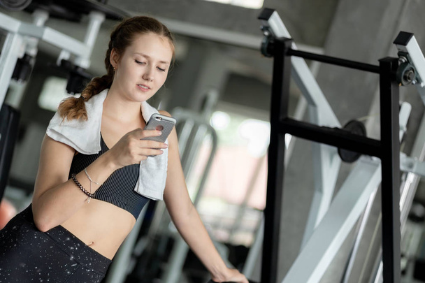 Happy Young attractive women fitness using smartphone resting in gym during morning exercise. Relaxation after hard workout in gym. Healthy sports lifestyle, Fitness concept. - Photo, image