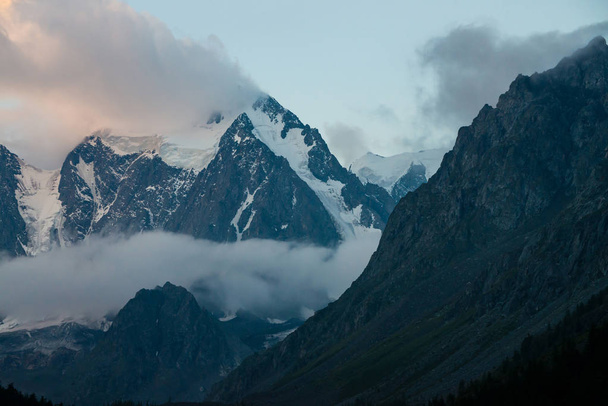 Low cloud before huge glacier. Giant snowy rocky mountains under cloudy sky. Thick mist in mountains at early morning. Impenetrable fog. Cold rocks. Dark atmospheric landscape. Tranquil atmosphere. - Photo, Image
