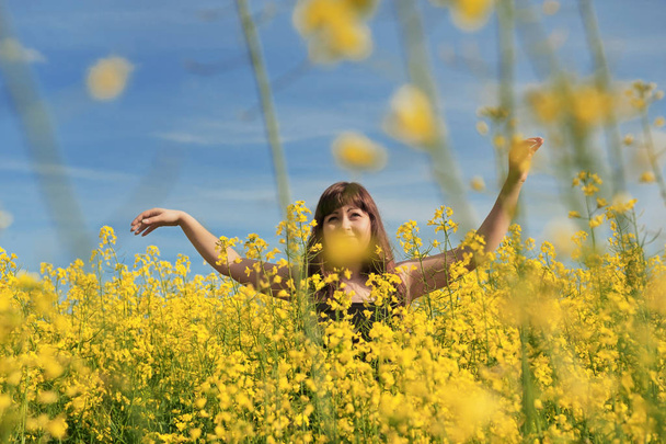 Young happy woman on summer day in the flower meadow and blue sky at the background. - Foto, Imagem