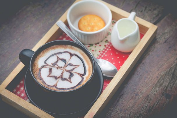 ζεστό καφέ με τέχνη γάλακτος από αφρό. Μαύρο φλιτζάνι καφέ. Ζεστός καφές - Φωτογραφία, εικόνα