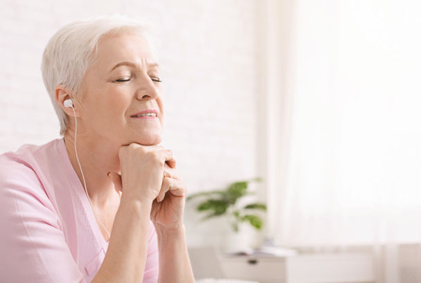 Mujer mayor disfrutando de la música en casa con los ojos cerrados
 - Foto, Imagen