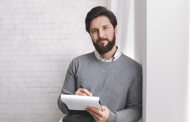 Friendly psychologist standing with clipboard, leaning at wall - Photo, Image