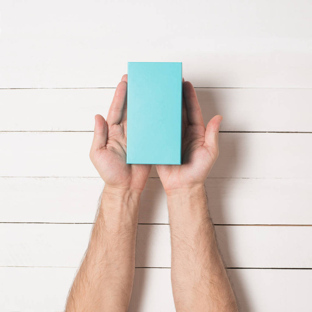 Rectangular turquoise box in male hands. Top view. White table on the background - Foto, afbeelding