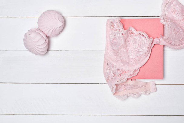 Pink lace bodice, notepad and marshmallow on white wooden background. Fashionable concept. - Photo, image