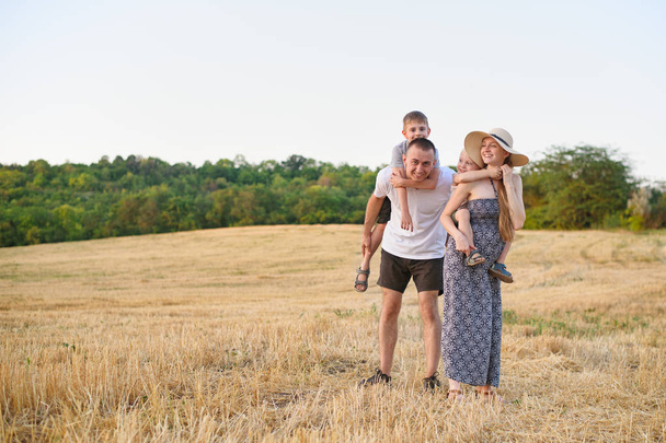 Happy young family. A father, a pregnant mother, and two little sons on their backs. Beveled wheat field on the background. Sunset time - Foto, Imagem