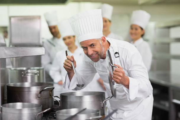 Head chef smelling pot of soup and smiling at camera in a commercial kitchen - 写真・画像