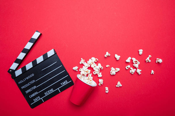 Clapperboard and pop corn on red color background, top view - Foto, imagen