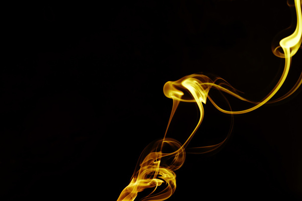 Vista del humo liso dorado que se enrolla a través de la oscuridad
 - Foto, imagen